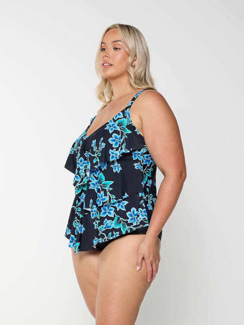 Blonde model shows side of tankini top with blue flowers and figure flattering ruffles