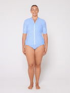Woman wearing a light blue rash top with a zipper on a white background