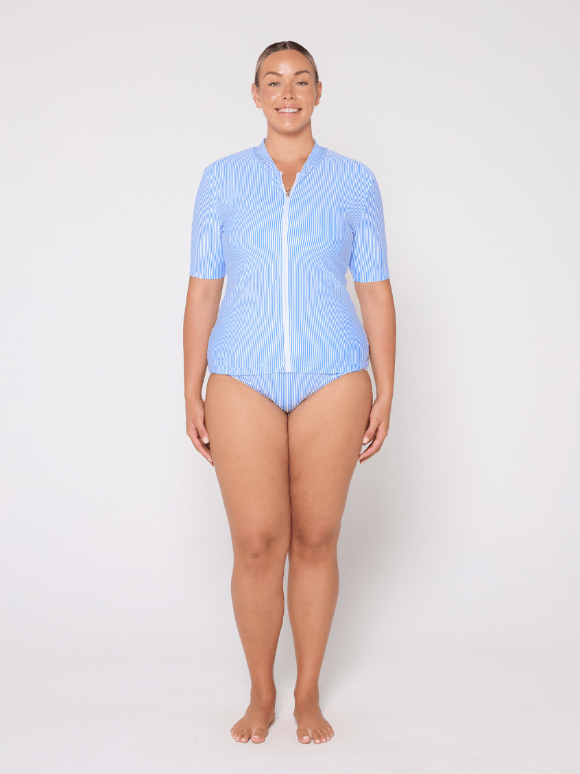 Woman wearing a light blue rash top with a zipper on a white background