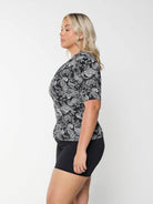 Side profile of blonde curve model in studio wearing short sleeve rash vest in chlorine resistant in paisley print