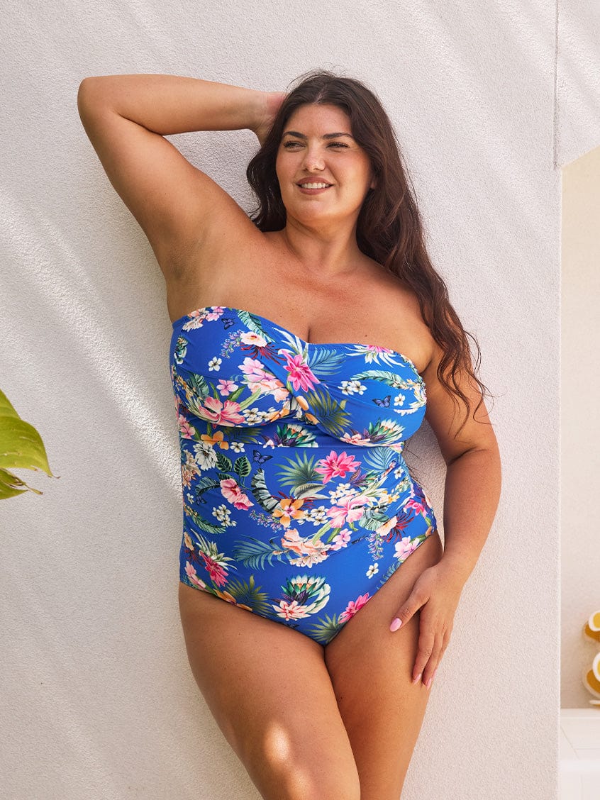 Brunette model wears flattering bandeau one piece in blue floral print with removable straps
