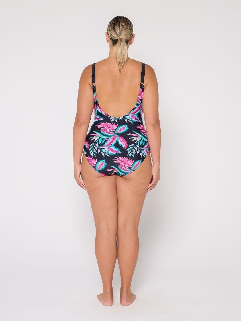 Woman wearing a tropical leaf patterned swimsuit with low socop back on a white background