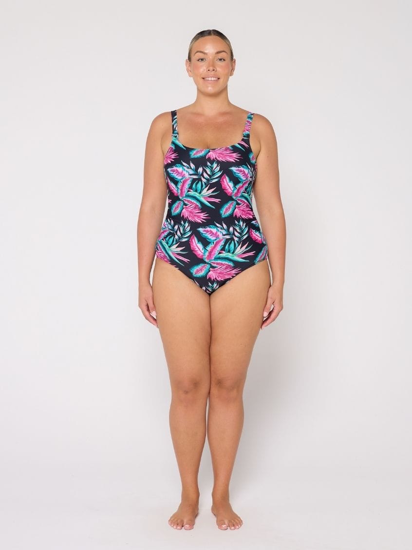 Woman wearing a tropical leaf patterned tank one piece swimsuit on a white background
