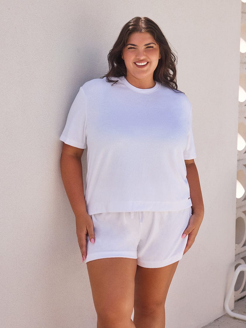 Woman wearing a white t-shirt and shorts against a light-colored wall.