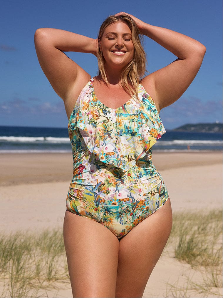 Woman in a floral swimsuit standing on a beach with ocean and sky in the background