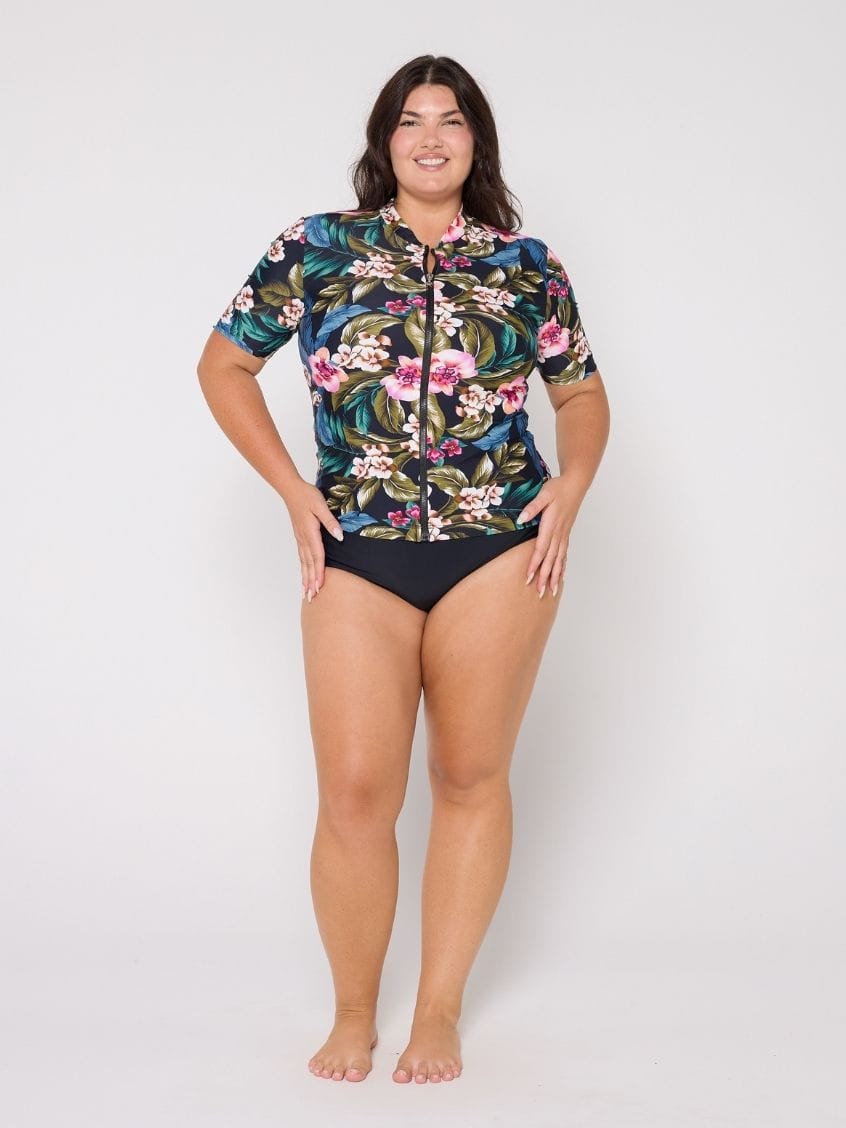Woman wearing a floral rash guard and black swimsuit bottoms on a white background