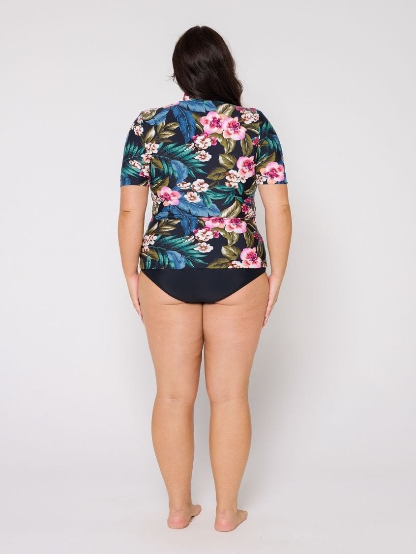 Person wearing a floral and leaf patterned rash top with a plain background