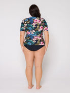 Person wearing a floral and leaf patterned rash top with a plain background