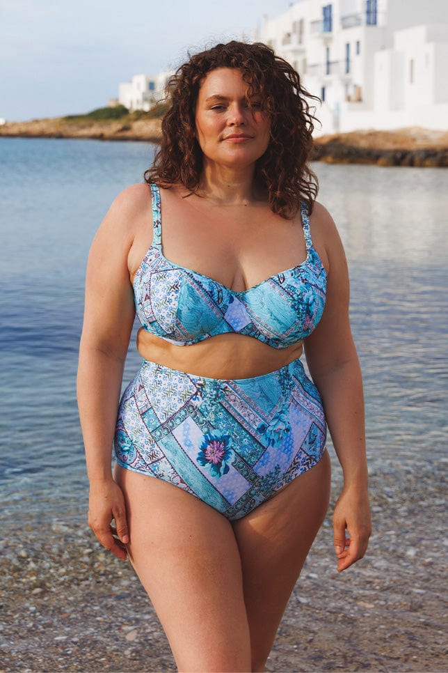 brunette model on the beach wearing a blue patchwork print underwire bikini top
