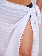 White sheer fabric with pom-pom trim draped over a person, on a neutral background