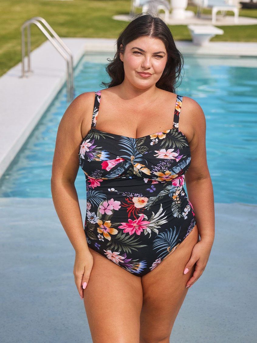 Brunette model wears chlorine resistant black floral one piece swimsuit with removable straps