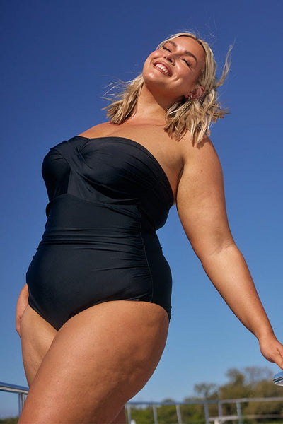 Blonde model wearing strapless black one piece swimsuit