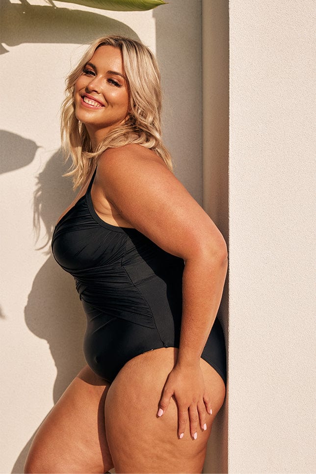 Blonde model showing side of black one piece swimsuit