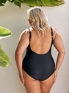 back of women wearing a black one piece swimsuit standing in front of a white wall