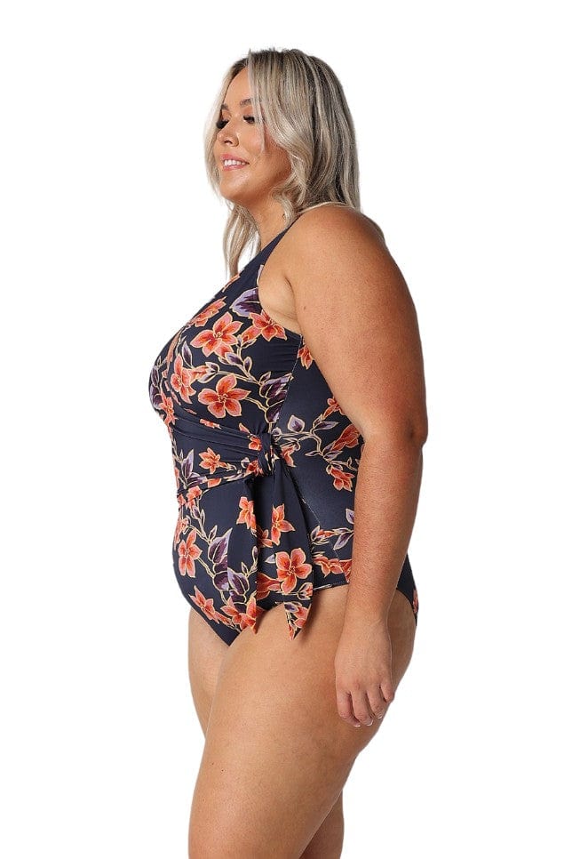 Side of blonde model in studio wearing a navy and orange floral one piece with tie side detail and v neckline