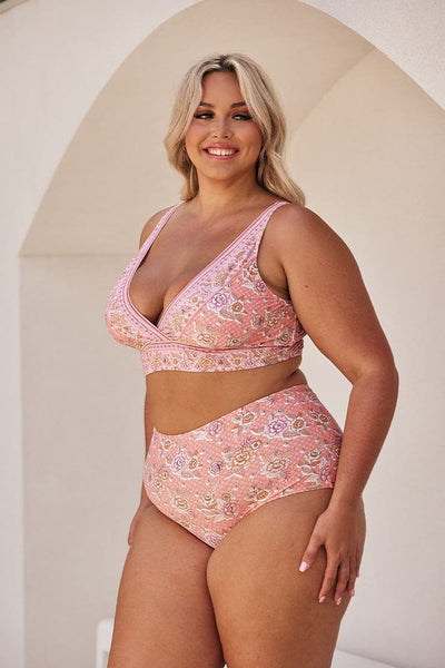 Blonde model showing side of light pink floral bikini top and high waisted pant