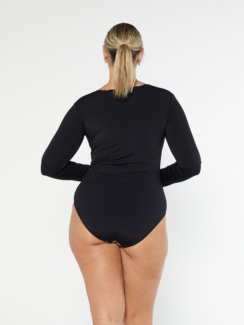Blonde model shows the back of black full coverage one piece with long sleeves