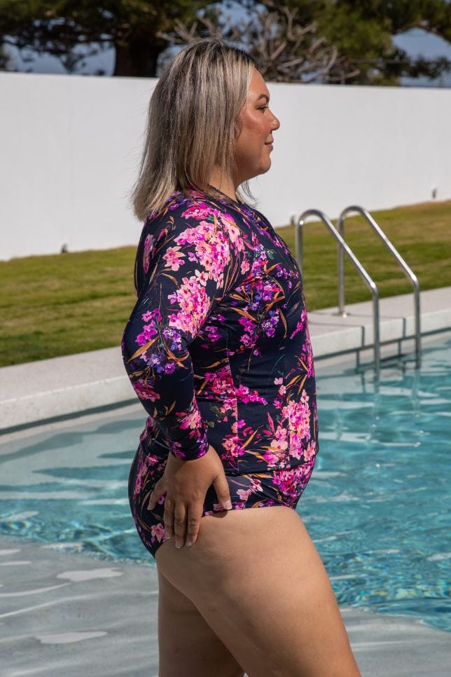 Side of model wearing zip front rash vest in pink and purple floral with long sleeves