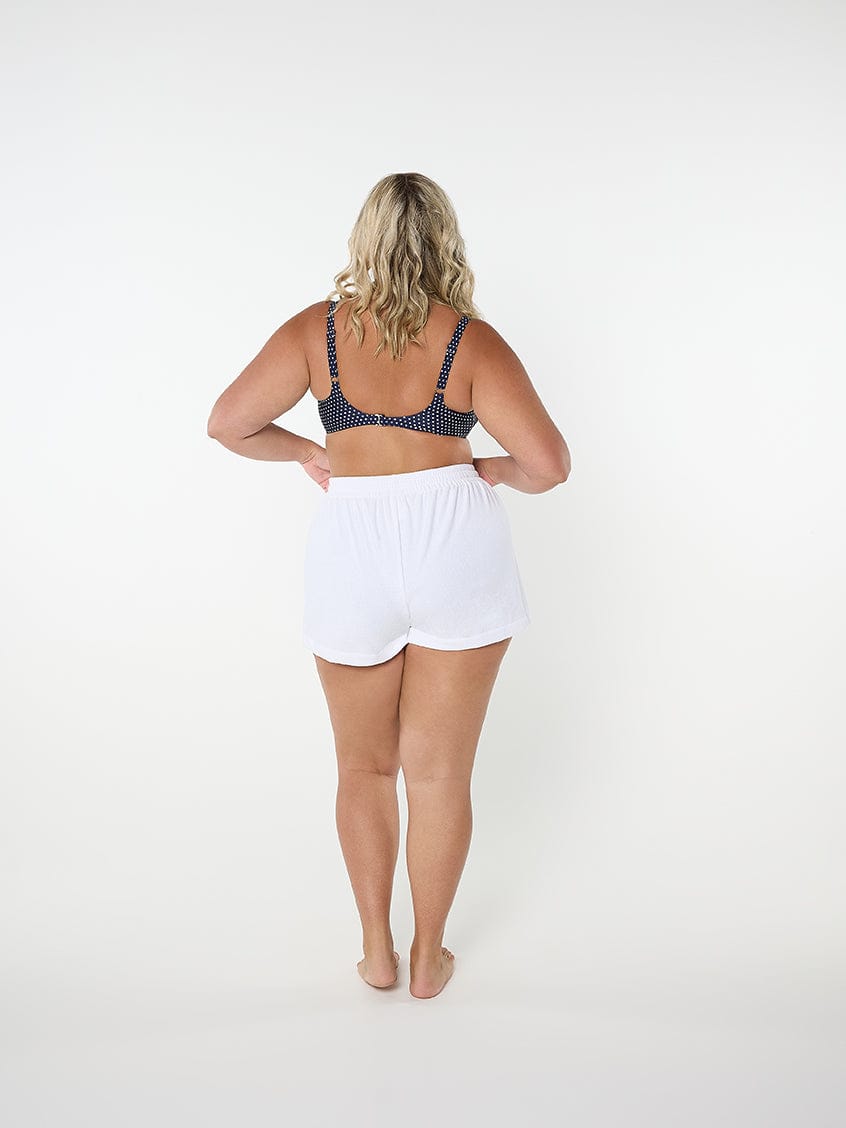 Woman wearing a polka dot bralette and white shorts on a white background