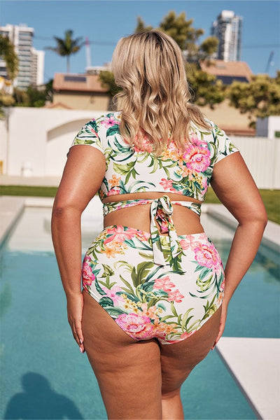 Blonde model showing back of white floral bikini set next to pool