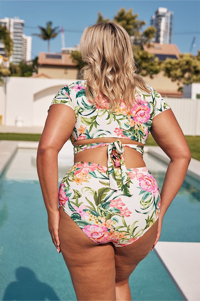 Blonde model showing back of white floral bikini set next to pool