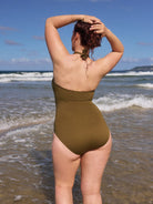 Person wearing a green swimsuit standing on a beach with ocean waves in the background