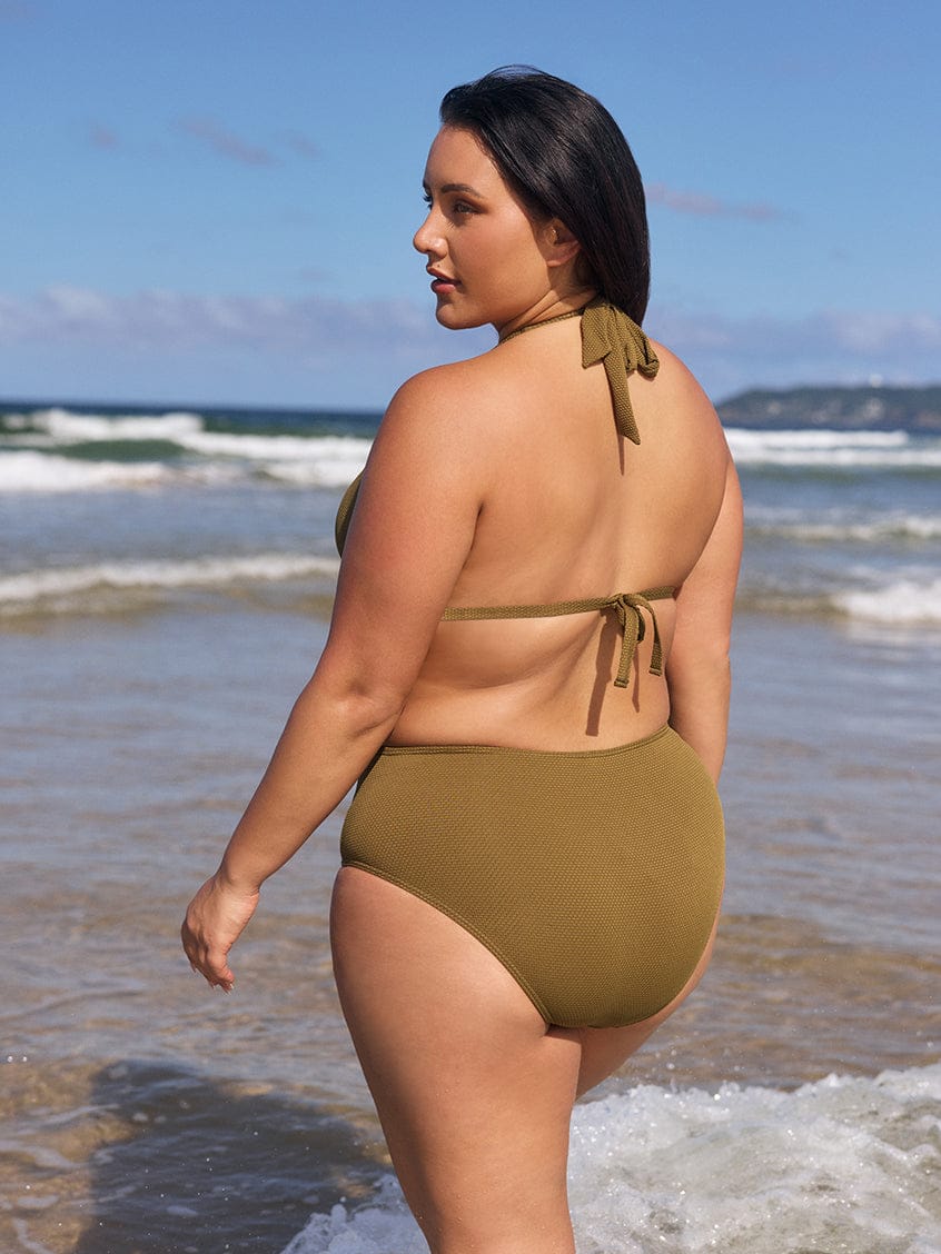 Woman in a green bikini standing on a beach with ocean waves in the background