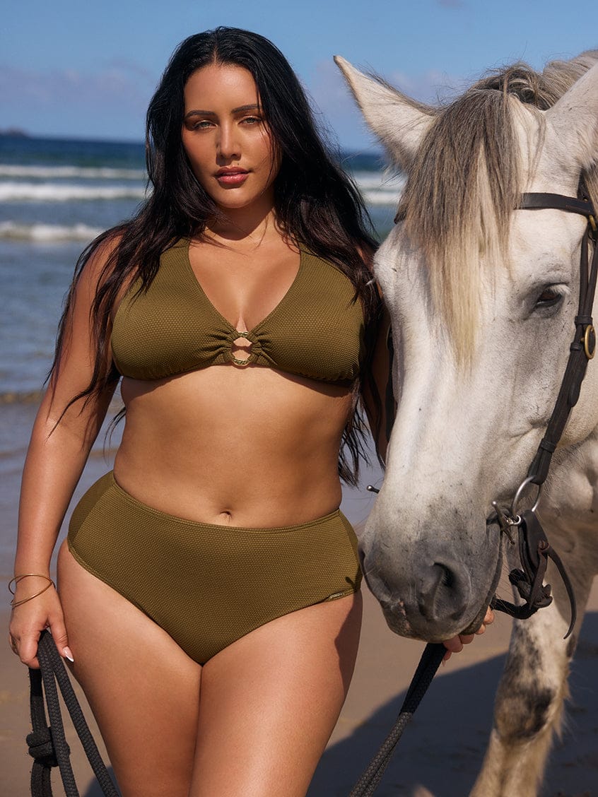 Woman in a green bikini standing next to a horse on a beach