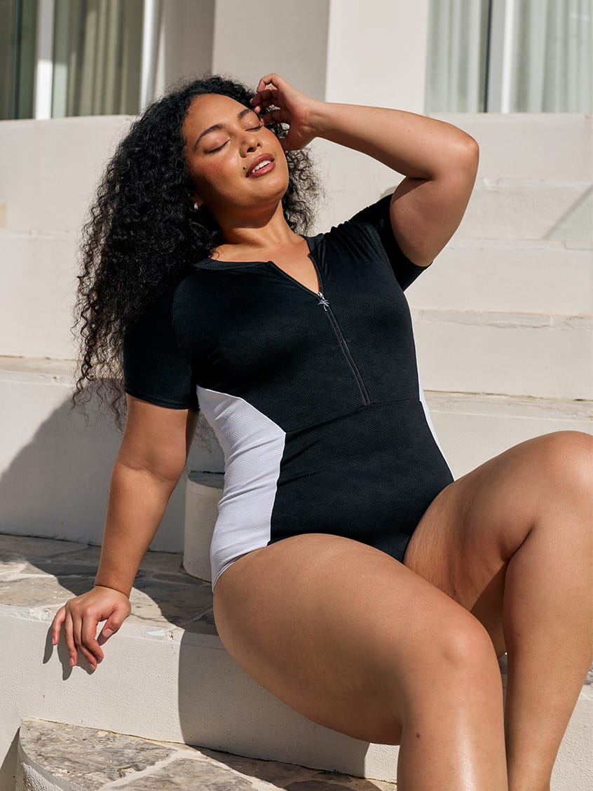 Close up image of model wearing a zip front detail one piece in black and white textured print