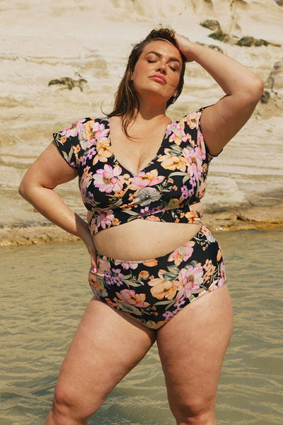 Brunette plus size model posing in water wearing orange and black high waisted pant