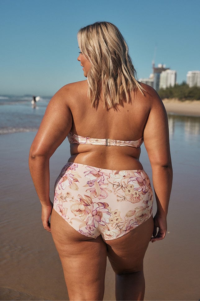 Blonde model showing back of pastel pink bikini bottoms on beach