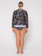 A woman viewed from the back wearing a long-sleeve floral swimshirt and matching bikini bottoms against a plain light gray studio background.