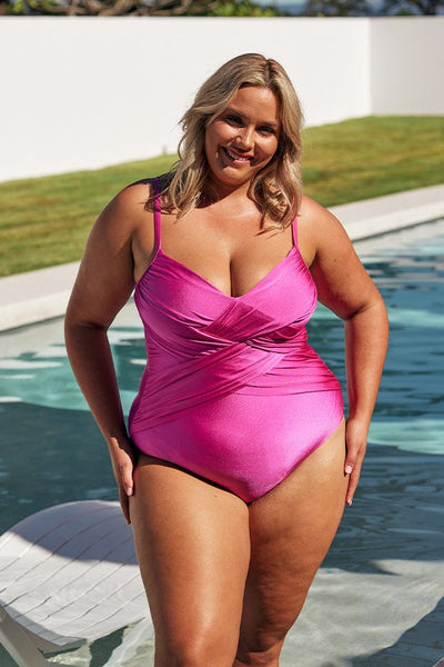 Blonde model wears metallic pink criss cross one piece next to pool