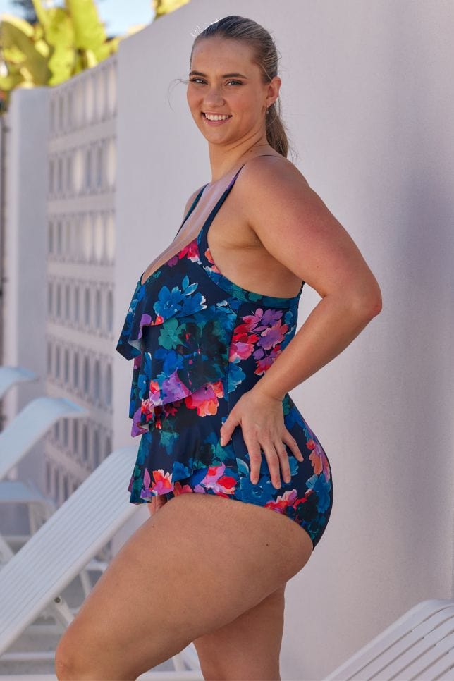 side profile of model wearing a navy floral one piece swimsuit with ruffle detail at the front