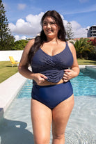 brunette model wearing navy high waisted swim bottoms with matching dotty tankini