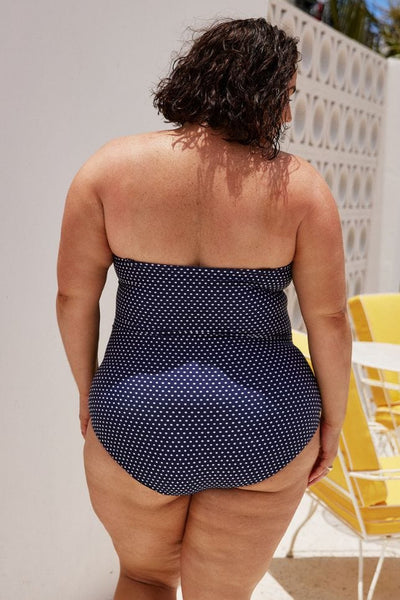 back of model wearing a navy and white polkadot one piece swimsuit