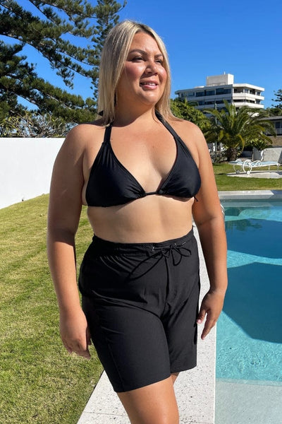 model standing in front of a pool wearing a black above knee boardshort with tie front detail