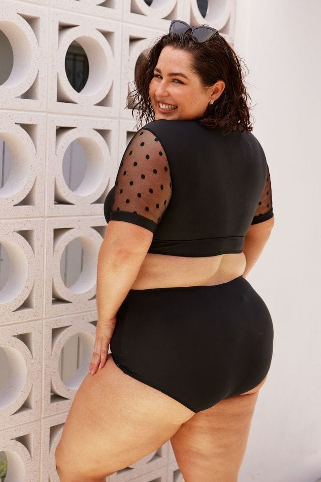 back of model wearing a black crop bikini top with mesh polkadot short sleeves