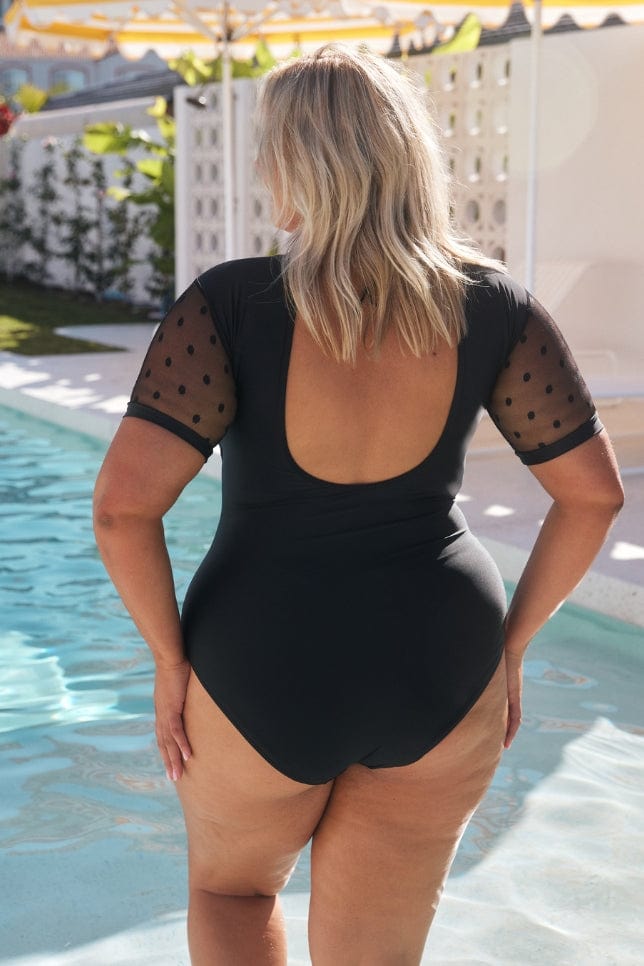 back of model wearing the black one piece with low scoop back and tie at the top of neck