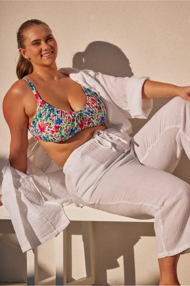 model sitting on a bench wearing a white cheesecloth set with the shirt open showing a floral bikini top