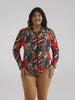 A woman modeling a long-sleeve, collared one-piece swimsuit with a colorful abstract print, standing against a plain light gray studio background.