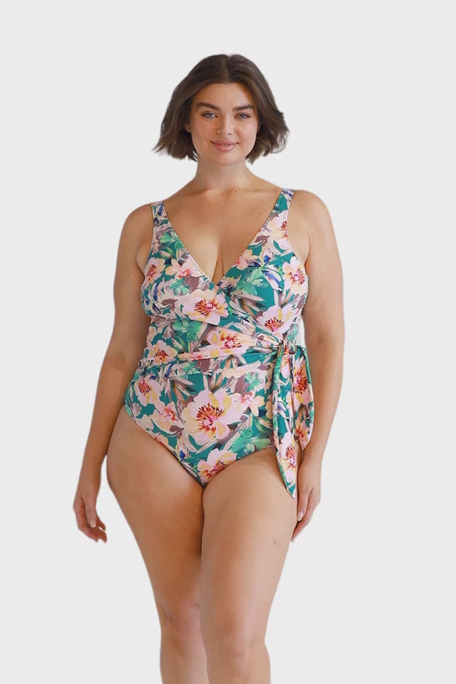 Curve model wearing wrap tie one piece with scoop back in green tropical floral print