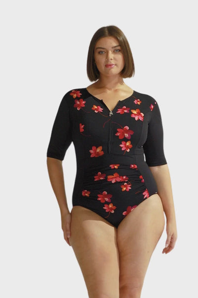 Brunette curve model wearing elbow length long sleeve one piece with zip front closure in black and pink flower print