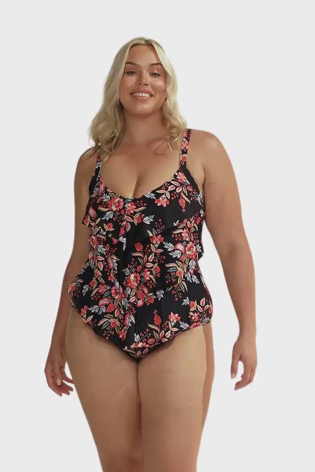 Blonde curvy model in studio wearing one piece with ruffle detail in pink and white floral print with black base