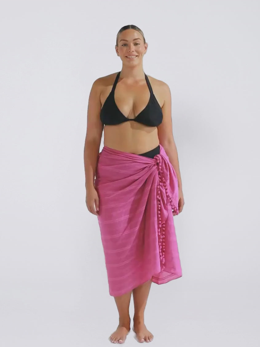 Blonde model wearing a plum colour sarong with pom poms in studio