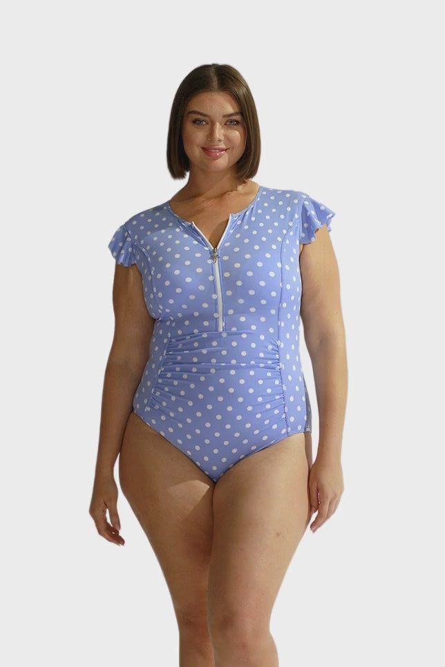 Brunette curve model wearing blue and white polkadot one piece with zip front and ruffle detail