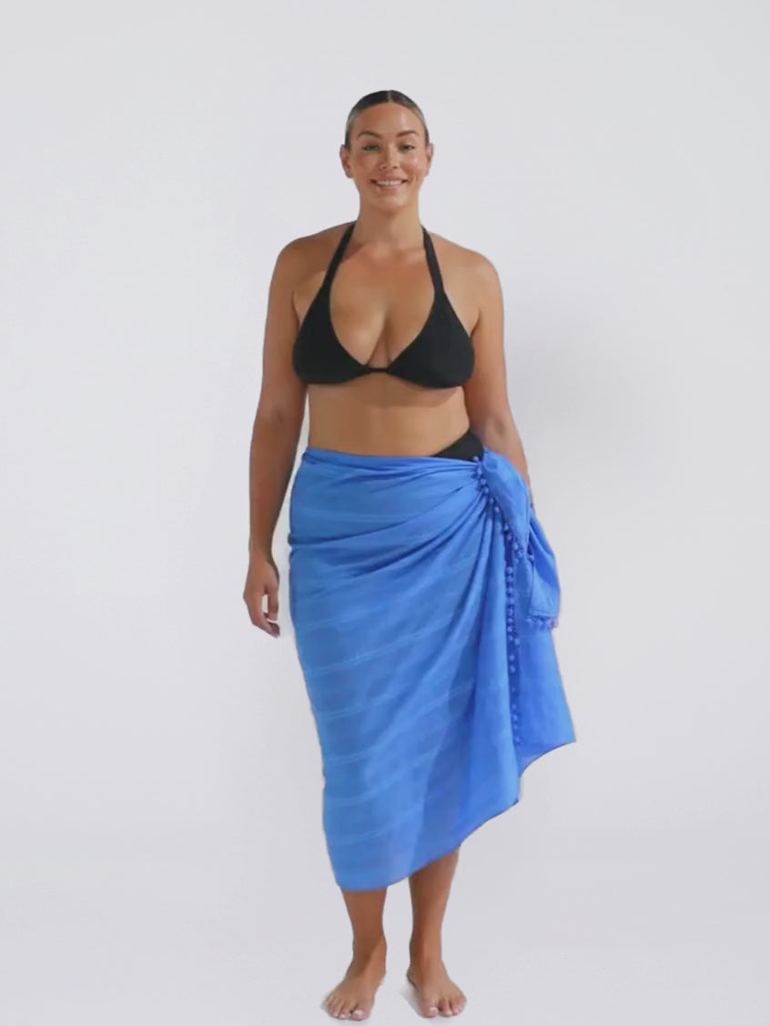 Blonde model in studio wearing a pom pom sarong in cobalt blue