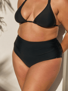 Person wearing black high-waisted bikini bottoms on a plain background