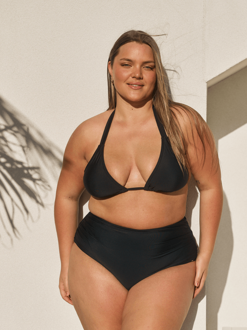 Person wearing black high-waisted bikini bottoms on a plain background