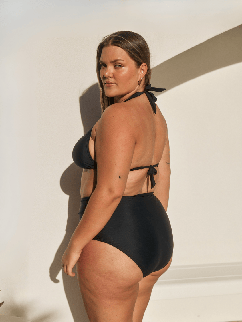 Person wearing black high-waisted bikini bottoms on a plain background